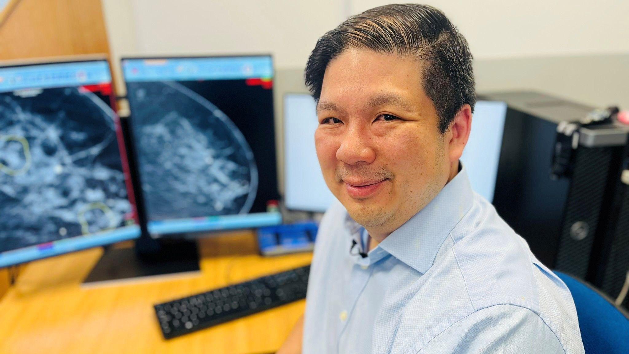 El profesor Gerald Lip vestido con una camisa azul claro con el cuello abierto y mirando a la cámara, frente a unas pantallas y un teclado.